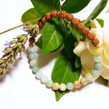 Close up of handmade Arogitā Bracelet – Amazonite & Rudraksha for Health & Happiness with Gardenia and lavender in background